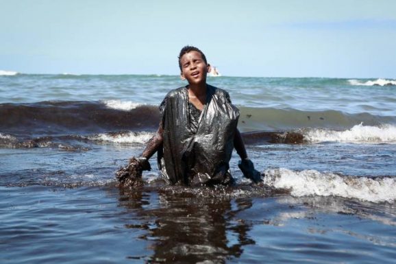 Everton Miguel dos Anjos, de 13 anos, o jovem que entrou no mar para retirar o óleo que se espalhava pela praia e foi fotografado coberto com o material negro e viscoso (Léo Malafaia/Folha de Pernambuco/Folhapress)/Folhapress)